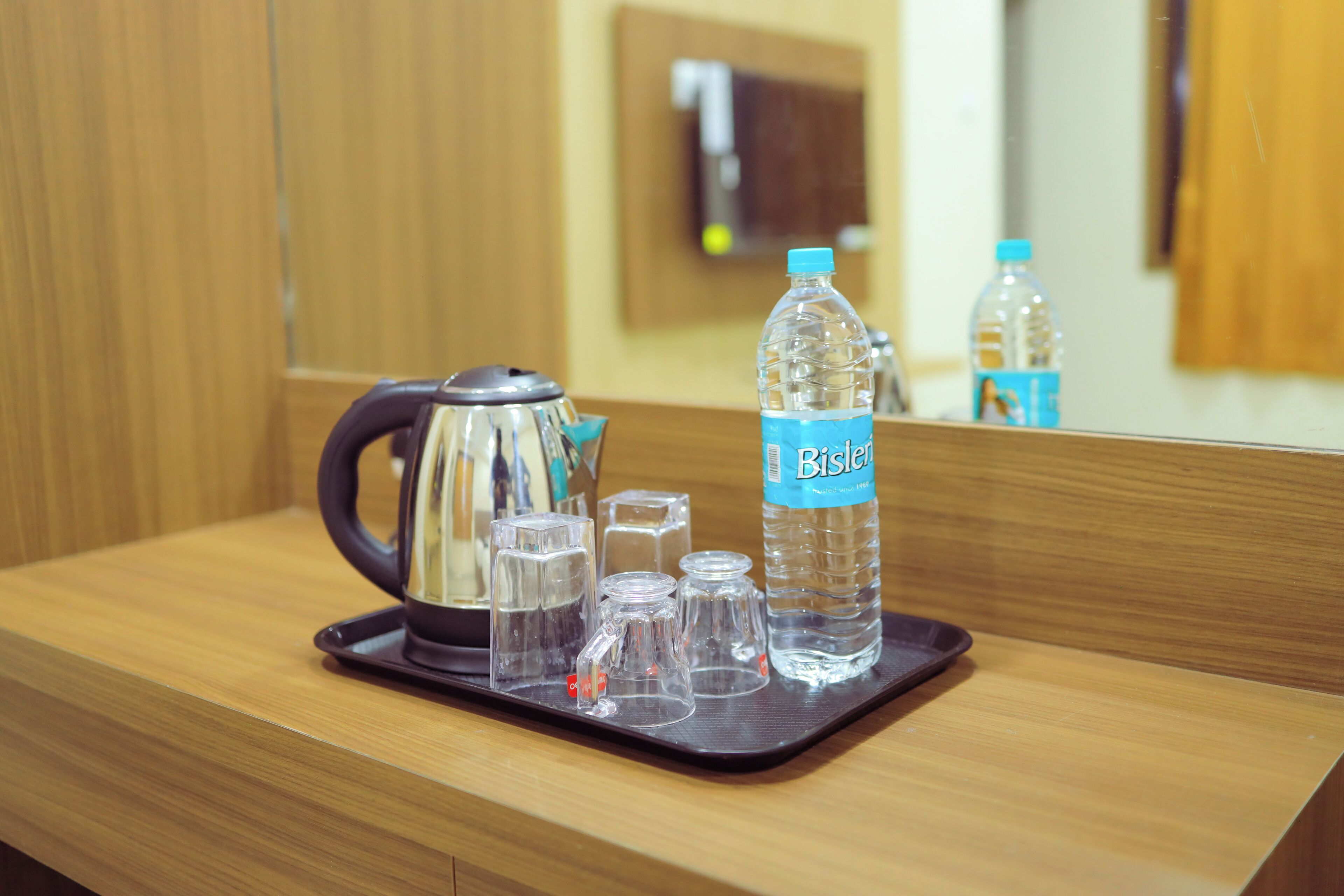 A wooden counter with a tray containing a water bottle, a kettle, and several glasses.