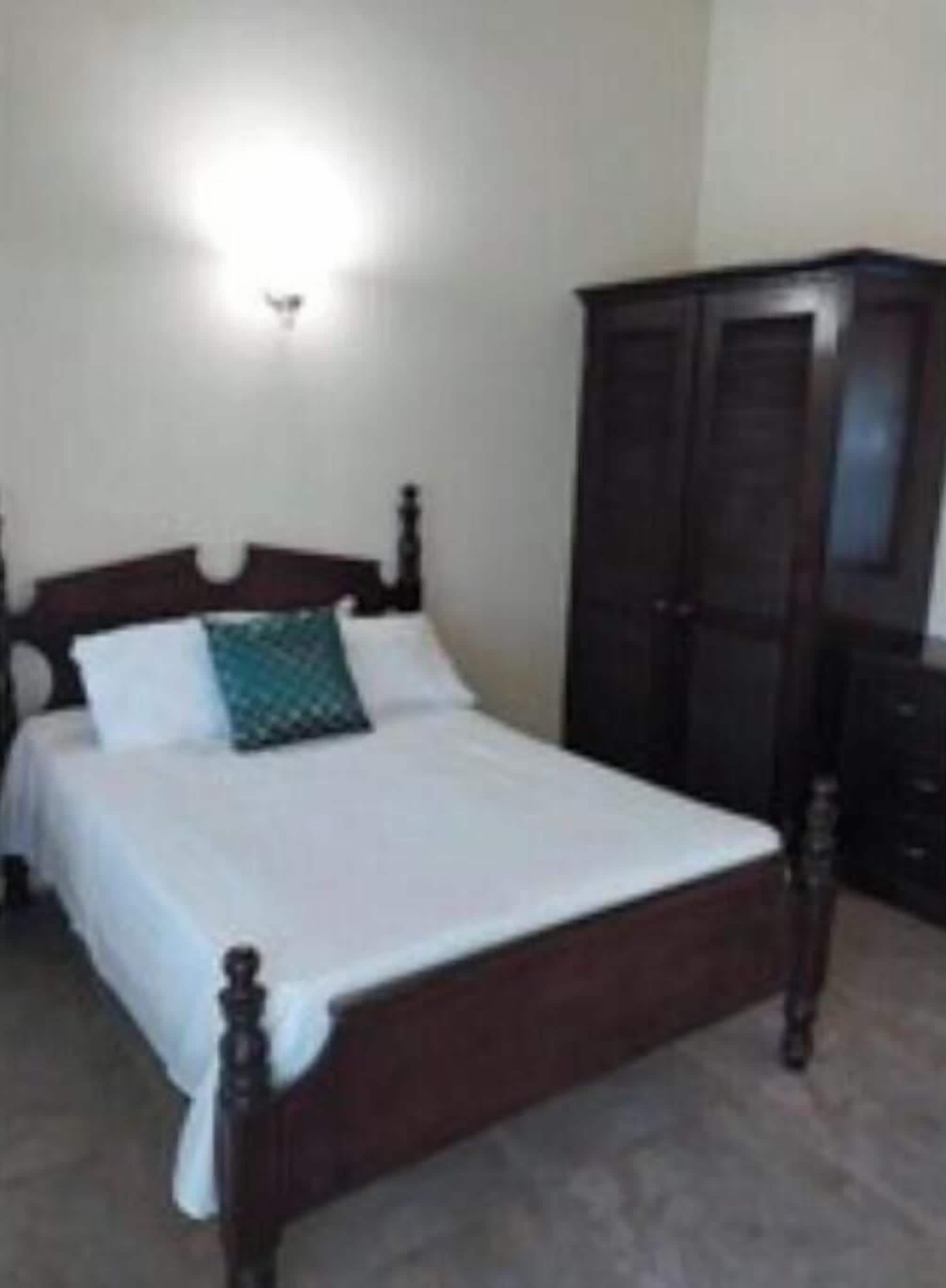 A bedroom with a wooden bed, white bedding, and a dark wooden wardrobe.