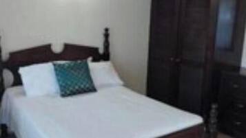 A bedroom with a wooden bed, white bedding, and a dark wooden wardrobe.