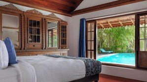 Une chambre dotée d’un grand lit, de meubles en bois, d’une vue sur une piscine et d’une fenêtre donnant sur un espace verdoyant.