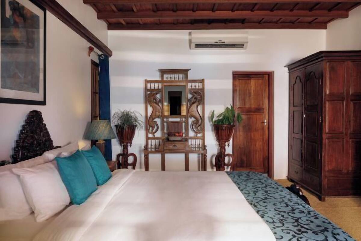 A room with a bed, a wooden cabinet, a mirror, and a table with a lamp and plants.