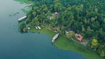 An aerial view of a coastal area with a dock, boats, and a small building surrounded by dense greenery.