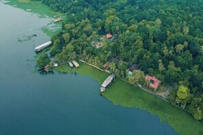 Vista aérea de una zona costera con un muelle, barcos y un pequeño edificio rodeado de abundante vegetación.