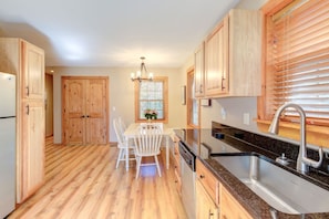 A kitchen with wooden cabinets, a granite countertop, a stainless steel sink, and a dining table with chairs.