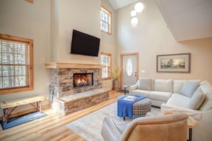 A living room with a stone fireplace, a flat-screen TV mounted above it, a sofa, a bench, and a door with a decorative glass window.