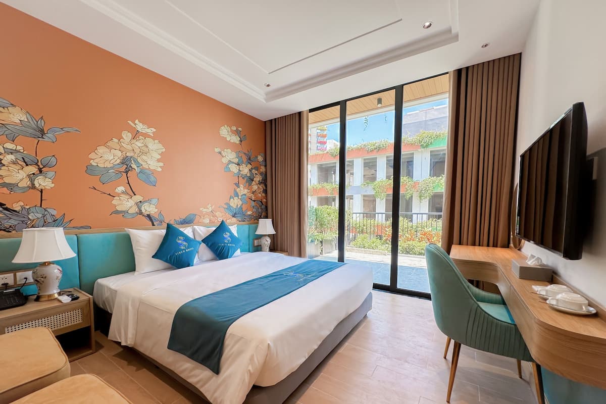 Een hotelkamer met een bed, een bureau, een stoel, een televisie en een balkon met uitzicht op gebouwen.