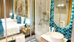 A modern hotel room with a glass-enclosed shower, a large bed with blue bedding, and a bathroom with a large mirror and a decorative backsplash. - SIREN HOTEL HAI TIEN (Hoang Tien)