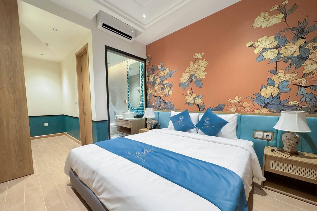 Een hotelkamer met een bed, een nachtkastje, een lamp, een badkamer met een spiegel en een bloemen behang.
