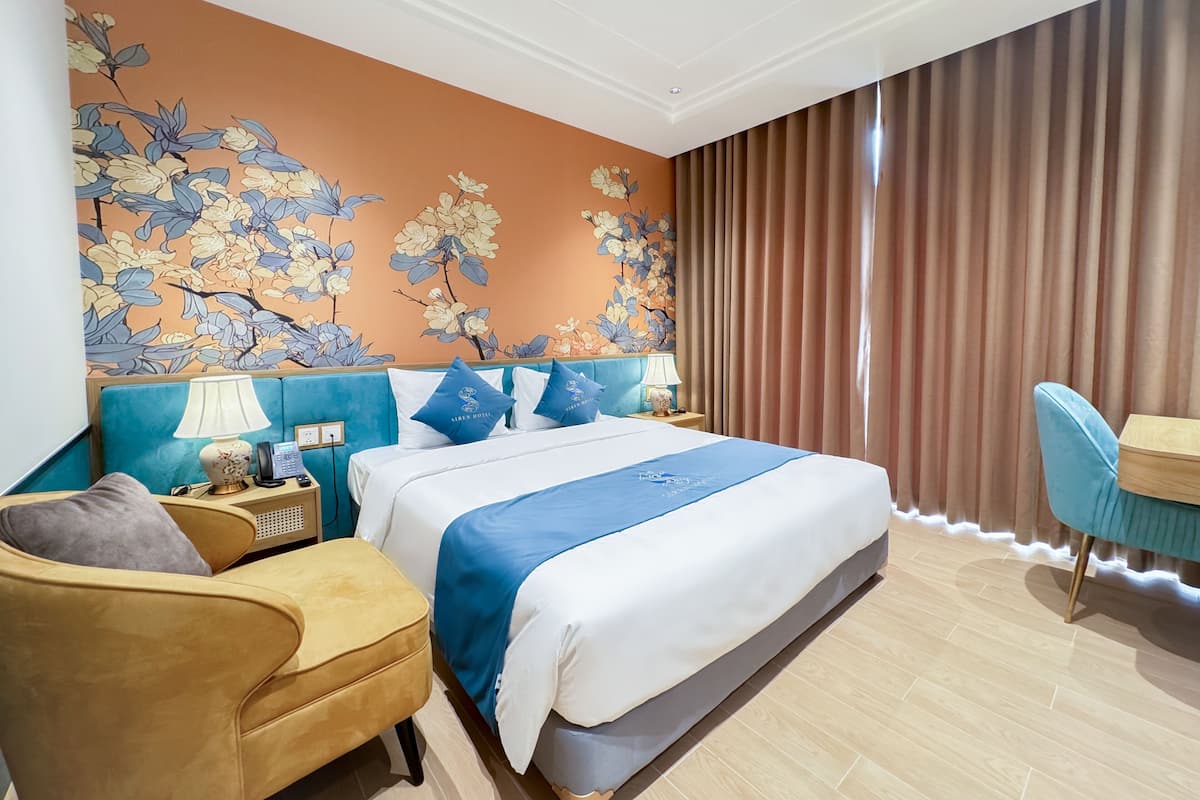 Een hotelkamer met een bed, bureau, stoel, nachtkastje met lamp en een bloemen behang.
