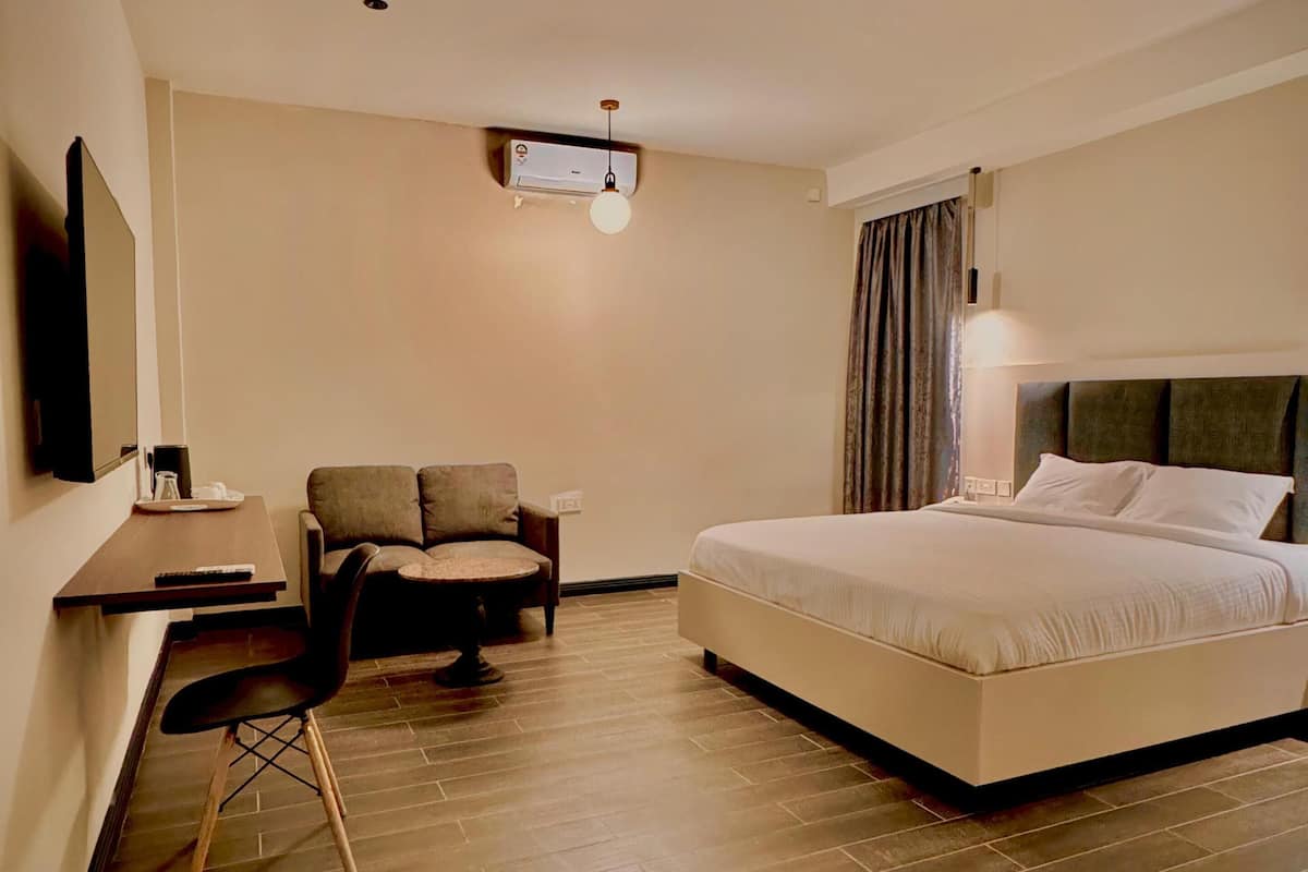 A hotel room with a bed, a desk with a chair, a TV, and a ceiling-mounted air conditioner.