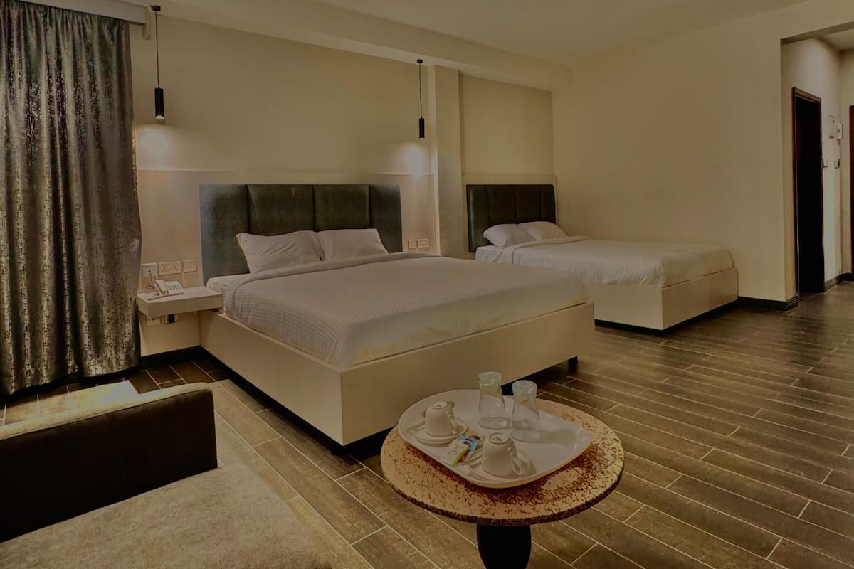 A hotel room with a large bed, a smaller bed, a round table with a tray of breakfast items, a sofa, and a hanging light fixture.