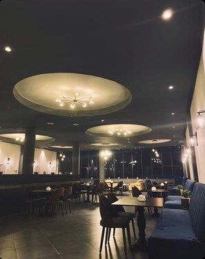 Un restaurant doté de nombreuses tables et chaises, de grands luminaires circulaires au plafond et d’un aménagement intérieur moderne.