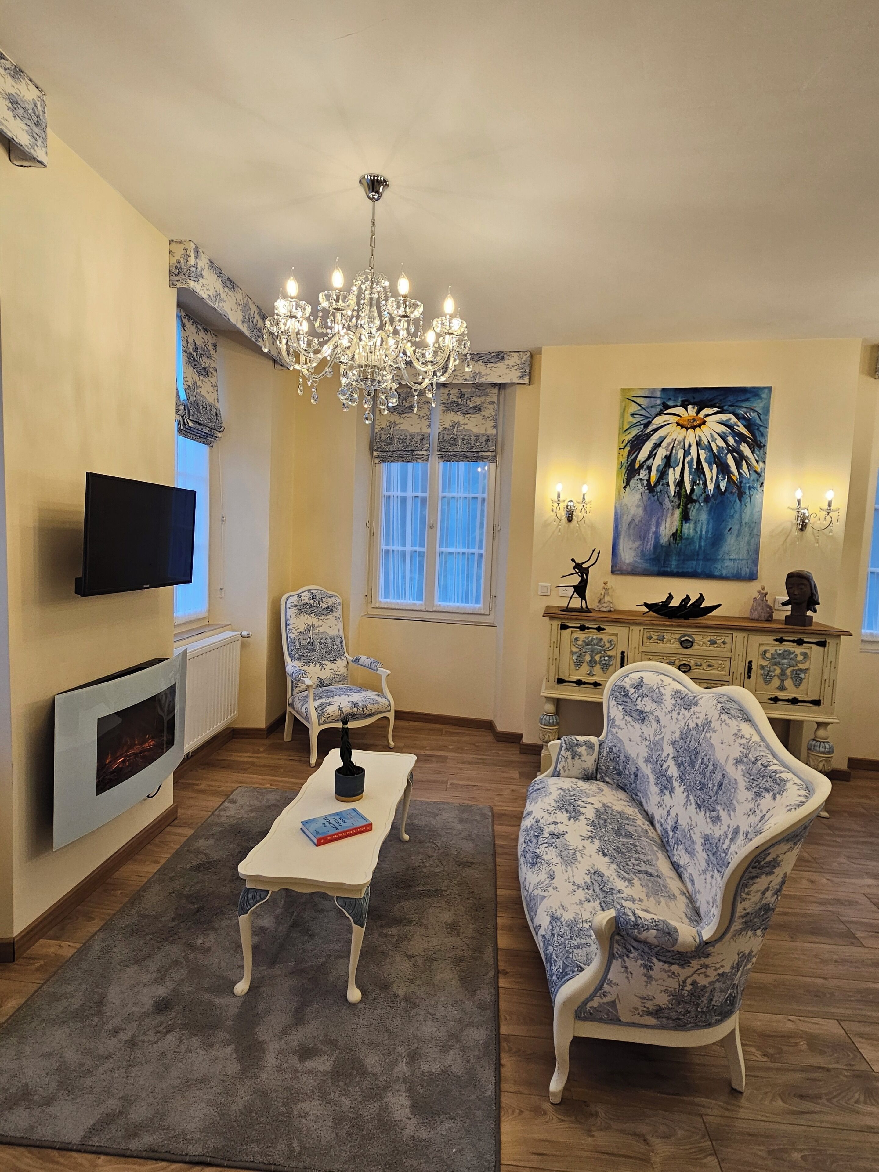Una sala de estar con chimenea, candelabro, televisor y un cuadro en la pared.