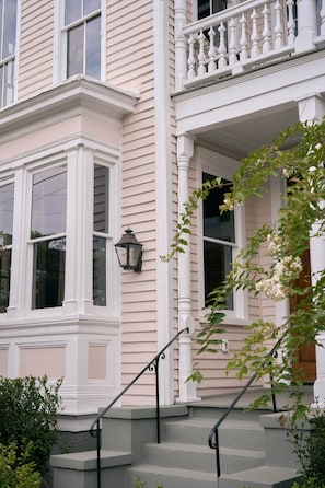 A two-story house with a front porch, a set of stairs, and a window with a white trim.
