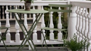 Uma mesa de metal verde com uma planta em vaso, um corrimão branco e um pilar branco.