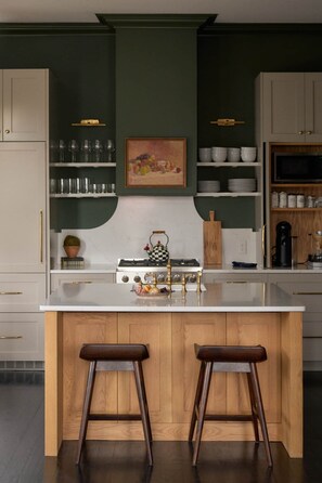 A kitchen with a central island, wooden stools, a stove, and various kitchenware.