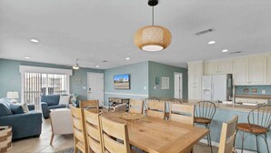A spacious living room with a wooden dining table, blue sofas, and a kitchen area with white cabinets. - Waterfront Gulf Shores Condo w/ Beach Access (Gulf Shores)