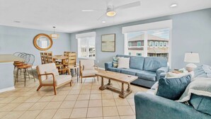 A spacious living room with a blue sofa, wooden coffee table, and a dining area with chairs and a table. - Waterfront Gulf Shores Condo w/ Beach Access (Gulf Shores)