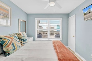 A bedroom with a bed, a ceiling fan, a window with blinds, and a door.
