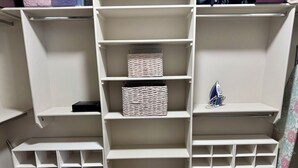 A white storage unit with multiple shelves and compartments, including a woven basket and an iron.