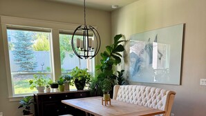 A dining area with a wooden table and bench, surrounded by potted plants and a large window.