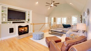 A spacious living room with a fireplace, a large flat-screen TV, a ceiling fan, and a cozy seating area with a sofa and ottomans. - Smith Mountain Lake Home w/ Private Hot Tub & Dock (Moneta)