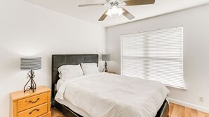 A bedroom with a bed, nightstands, a ceiling fan, and a window with blinds.