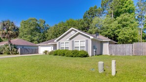 A single-story house with a front yard, a wooden fence, and a palm tree.