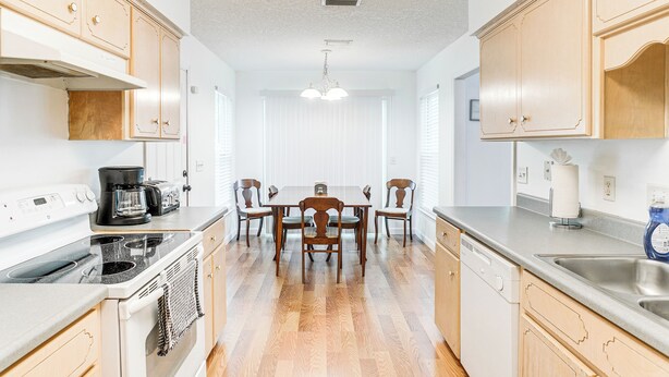 A kitchen with wooden cabinets, a dining table with chairs, a stove, and a dishwasher.
