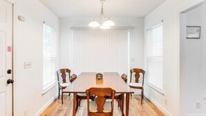 A dining room with a wooden table and chairs, white walls, and a ceiling light fixture.
