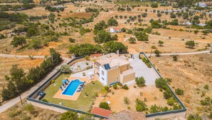 An aerial view of a residential area with a modern house featuring a swimming pool, surrounded by dry, hilly terrain and sparse vegetation. - Villa with heatable saltwater pool in Galé (Albufeira)