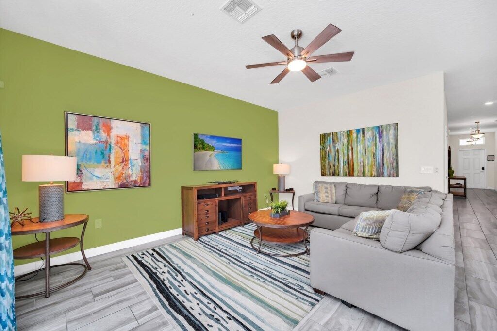 A living room with a green accent wall, a ceiling fan, and a gray sofa.