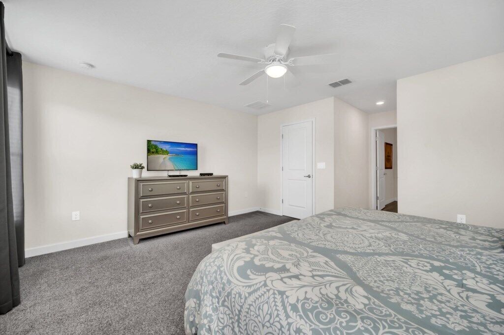 Un dormitorio con cama, cómoda, televisor y ventilador de techo.