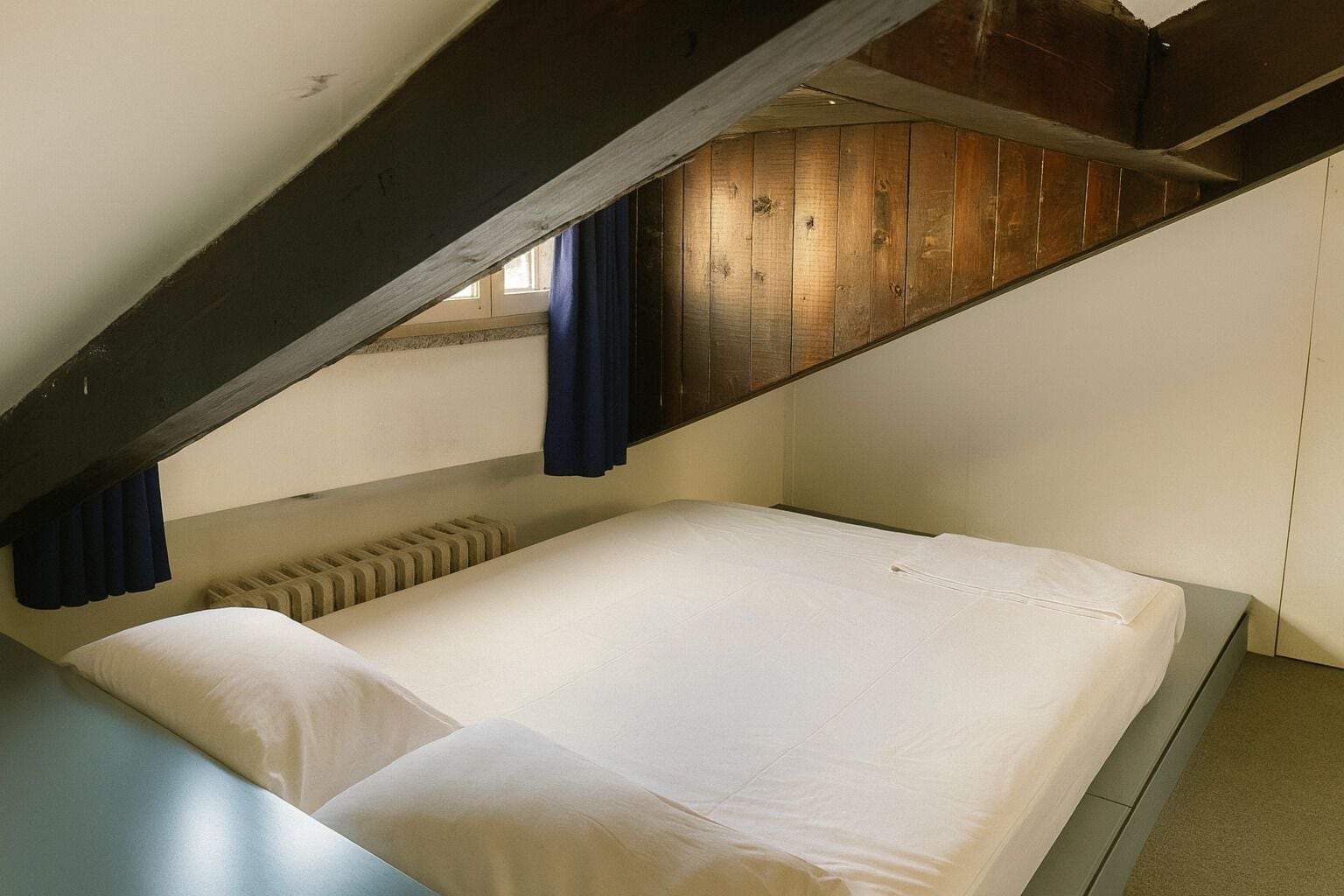 Ein kleines Zimmer mit einem Einzelbett, schrägen Wänden und Holzbalken.