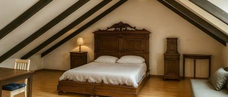 Un dormitorio con una cama de madera, una mesita de noche, una silla, un sofá y un armario alto de madera.