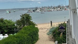 A beach view with a dock and boats, a sandy path, and a sign for 'Coyote Kayaks'. - Modern beachfront condo with private deck, harbor views, and parking! (Provincetown)
