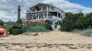A multi-story beachfront property with a prominent tower, balconies, and a sandy beach area. - Modern beachfront condo with private deck, harbor views, and parking! (Provincetown)