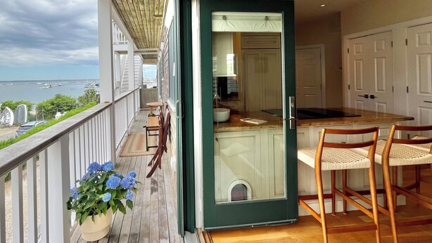 A balcony with a view of the sea, a wooden deck, and a dining area with chairs and a table. - Modern beachfront condo with private deck, harbor views, and parking! (Provincetown)