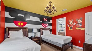 A hotel room with two beds, a chandelier, Mickey Mouse wall art, and a red accent wall.
