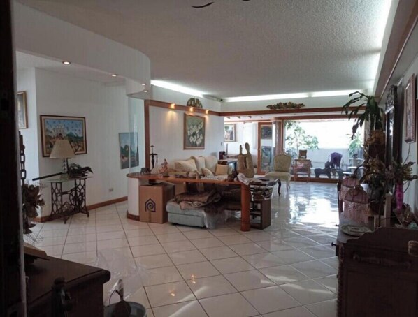 Relax in this spacious living area with a comfortable sofa set, coffee table, and dining table, surrounded by framed artwork and a large window offering a view of the outdoors.