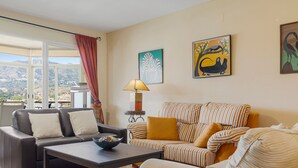 A living room with a sofa, armchair, and a coffee table. There is a window with a view of mountains. - Los Boliches Sunny Apartment - Ref 120 (Fuengirola)