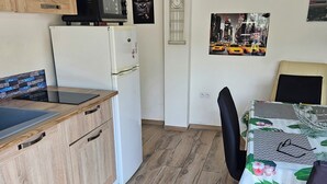 Eine kleine Küche mit Holzausstattung, einem weißen Kühlschrank, einer Mikrowelle und einem Essbereich mit einem Tisch, der mit einer blumigen Tischdecke bedeckt ist.