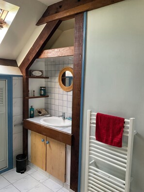 Ein Badezimmer mit einem Holzkosmetikschrank, einem weißen Waschbecken, einem Spiegel und einem roten Handtuch auf einer weißen Heizung.