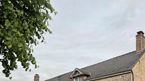 A stone building with a sloped roof, a small balcony, and a garden with flowers and a pathway. - Farmhouse in the heart of the Loire castles (VILLEMARDY)