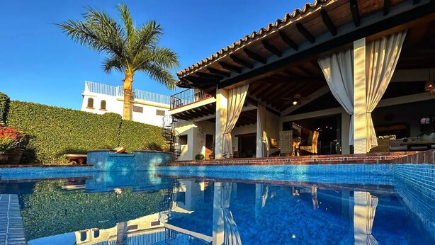 Une piscine avec un bord carrelé, un palmier et un bâtiment doté d’un balcon.