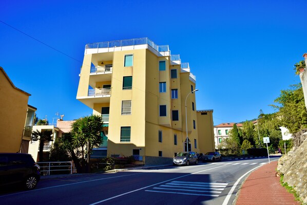 A yellow multi-story building with balconies, a pedestrian crossing, and parked cars. - Panorama Apartment in Ospedaletti by Wonderful Italy (Ospedaletti)