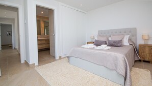 A bedroom with a bed, nightstands, and a bathroom visible through an open door. - Villa 142 Bahia de las Rocas (Manilva)