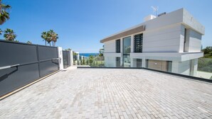 A modern building with a flat roof, large glass windows, and a view of the ocean. - Villa 142 Bahia de las Rocas (Manilva)