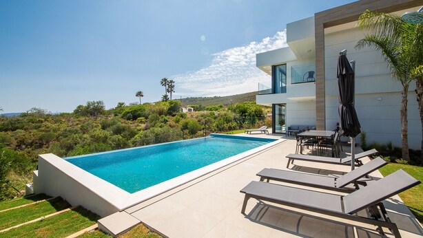 A modern outdoor pool area with a clear blue pool, lounge chairs, and a dining table. - Villa 142 Bahia de las Rocas (Manilva)