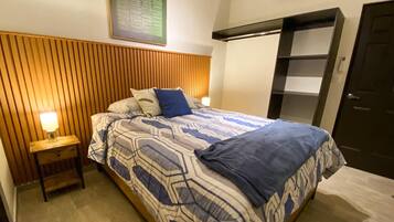 Una habitación de hotel con cama, mesita de noche, aire acondicionado de pared y una puerta.